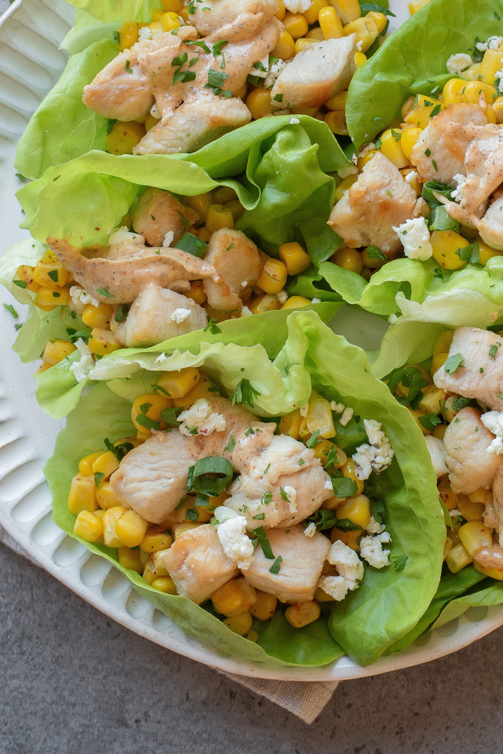 Four Street Corn Chicken Lettuce Wraps filled with diced chicken, corn, and crumbled cheese are arranged on a white plate.
