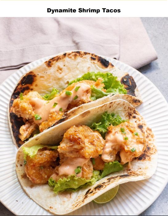 Two flour tortillas filled with fried shrimp, lettuce, and creamy sauce, served on a white plate.
