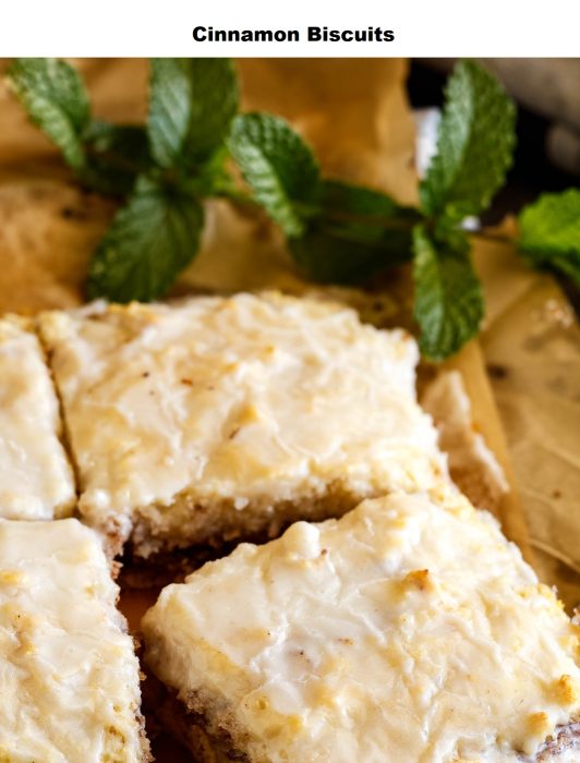 Iced cinnamon biscuits cut into squares on parchment paper, with fresh mint sprigs placed nearby.