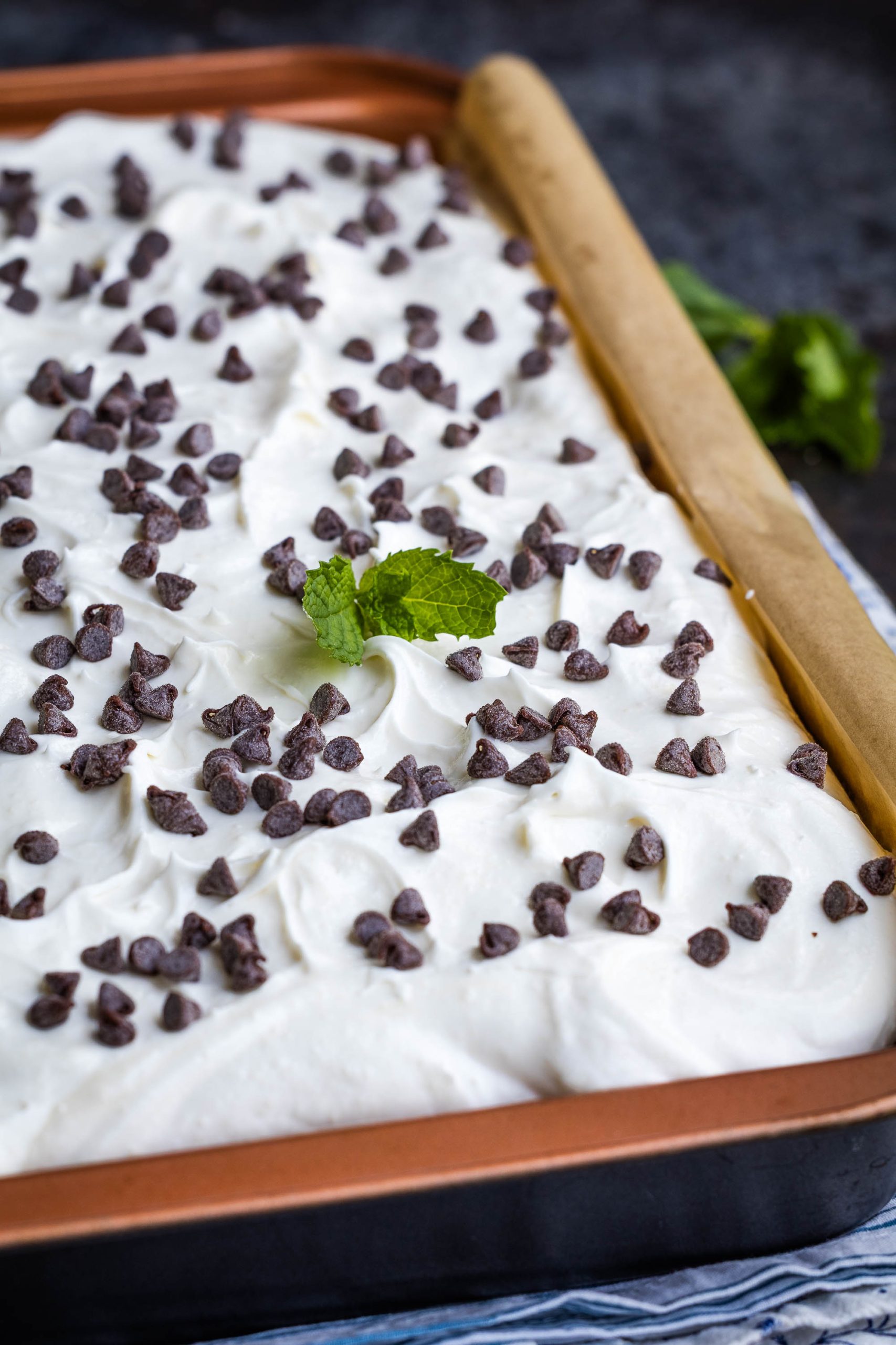 A rectangular pan of whipped cream dessert topped with chocolate chips and garnished with a sprig of mint.