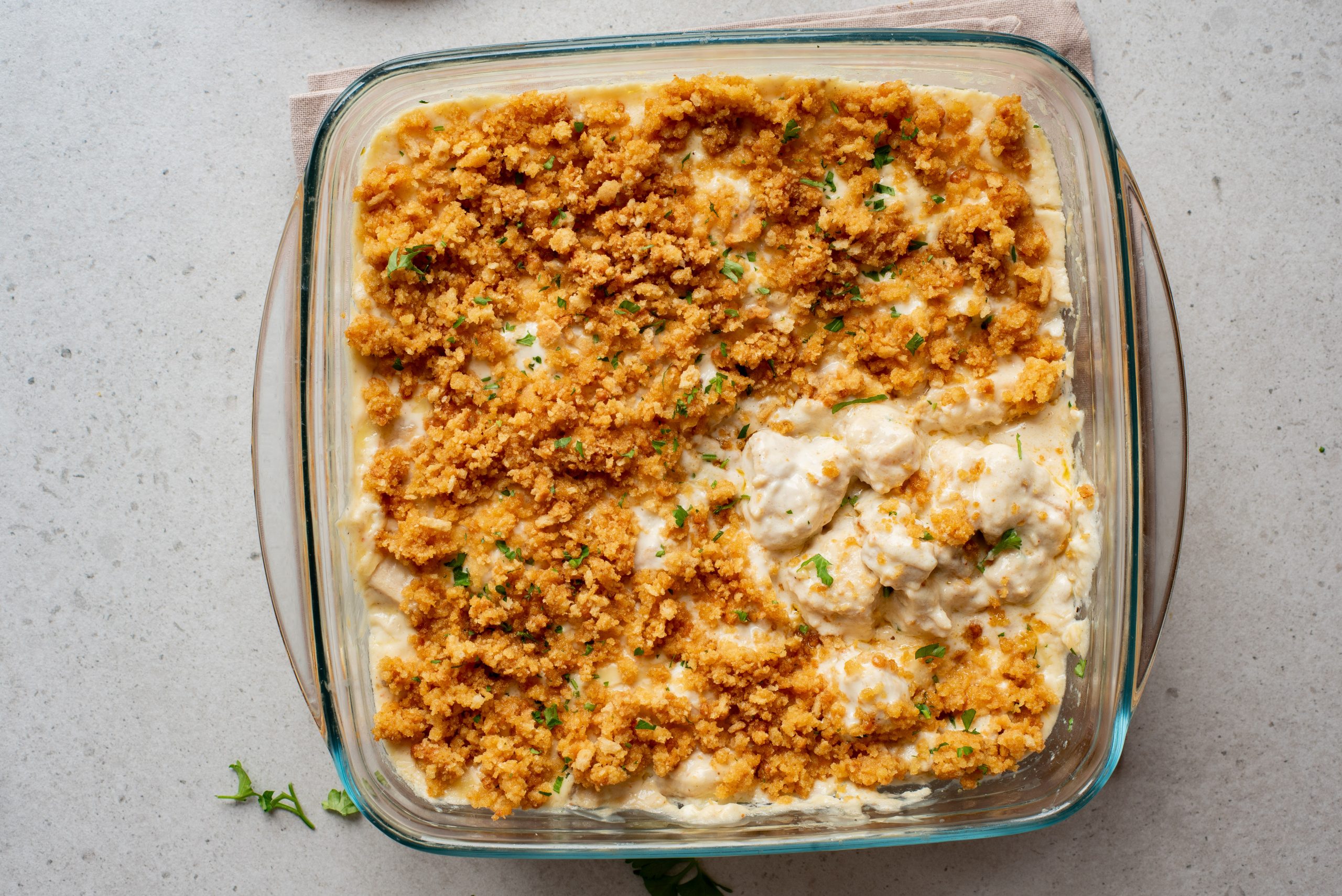A glass baking dish filled with creamy casserole topped with a layer of golden brown breadcrumbs and garnished with chopped parsley.