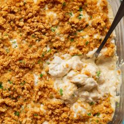 Glass baking dish filled with creamy casserole topped with golden-brown breadcrumbs; a serving has been scooped out with a spoon.