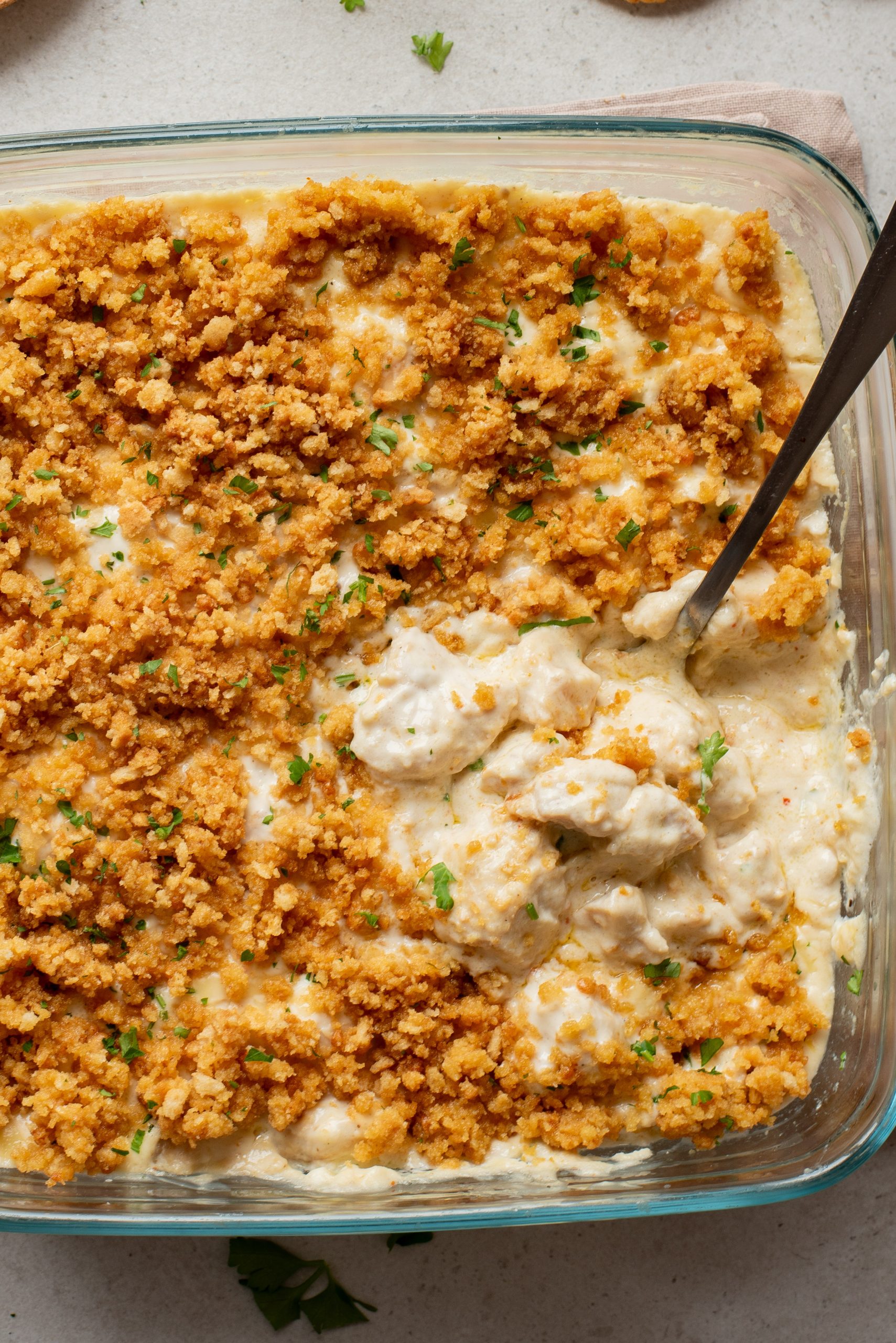 Glass baking dish filled with creamy casserole topped with golden-brown breadcrumbs; a serving has been scooped out with a spoon.