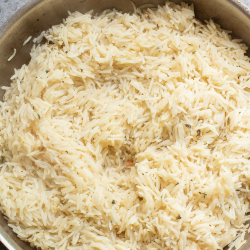 A pan filled with cooked rice sits on a gray countertop. Text reads: "How to make rice & pasta healthier. Paula's Picks easy hack.