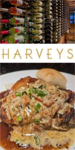 A wall lined with wine bottles, a sign reading "HARVEYS," and a plate of grilled chicken topped with creamy sauce and green onions, served with a roll at Harvey's Tupelo MS.