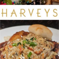 A wall lined with wine bottles, a sign reading "HARVEYS," and a plate of grilled chicken topped with creamy sauce and green onions, served with a roll at Harvey's Tupelo MS.