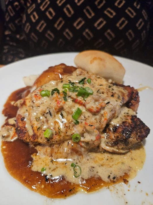 Grilled chicken topped with creamy sauce and green onions, served with mashed potatoes, brown gravy, and a bread roll on a white plate.