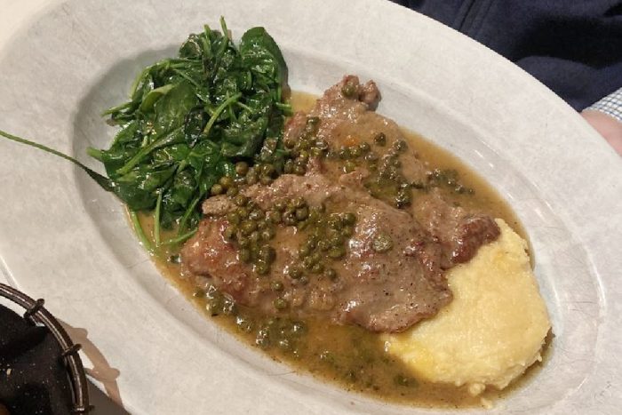 A plate with sautéed spinach, two pieces of meat in a caper sauce, and a serving of creamy mashed potatoes.