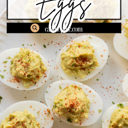 A plate of deviled eggs topped with paprika sits on a cloth napkin, with a fork and a lime in the background.