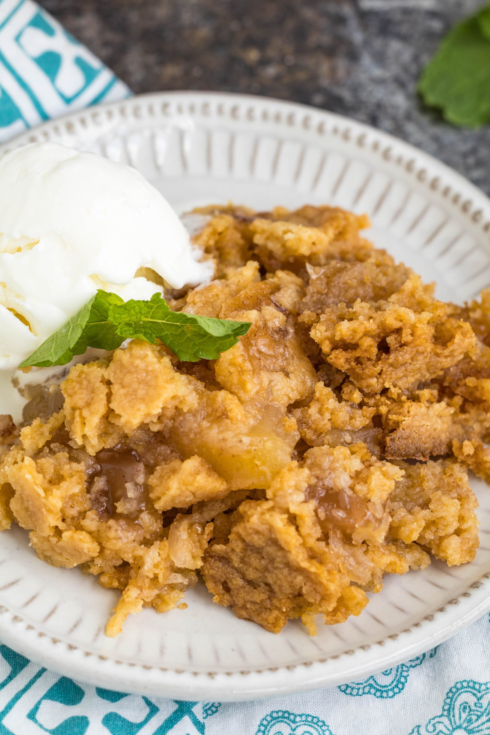 A serving of apple crumble with a scoop of vanilla ice cream and a mint leaf garnish on a white plate.
