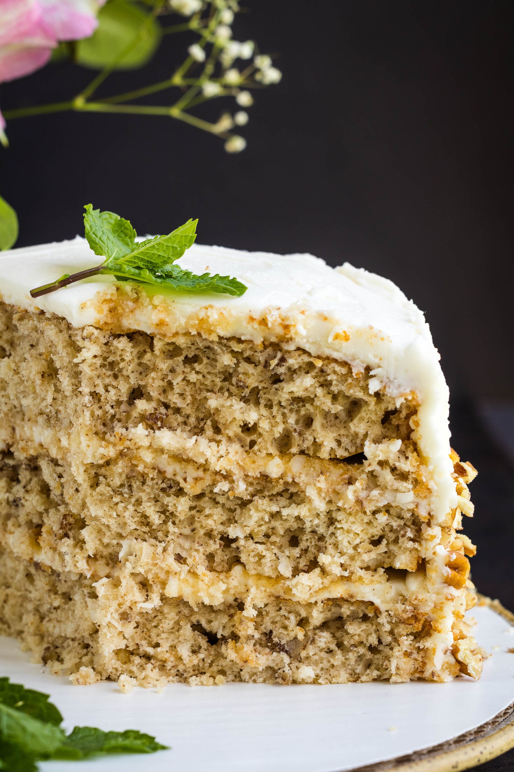 A close-up of a three-layer slice of cake with white frosting, garnished with a sprig of mint on top.