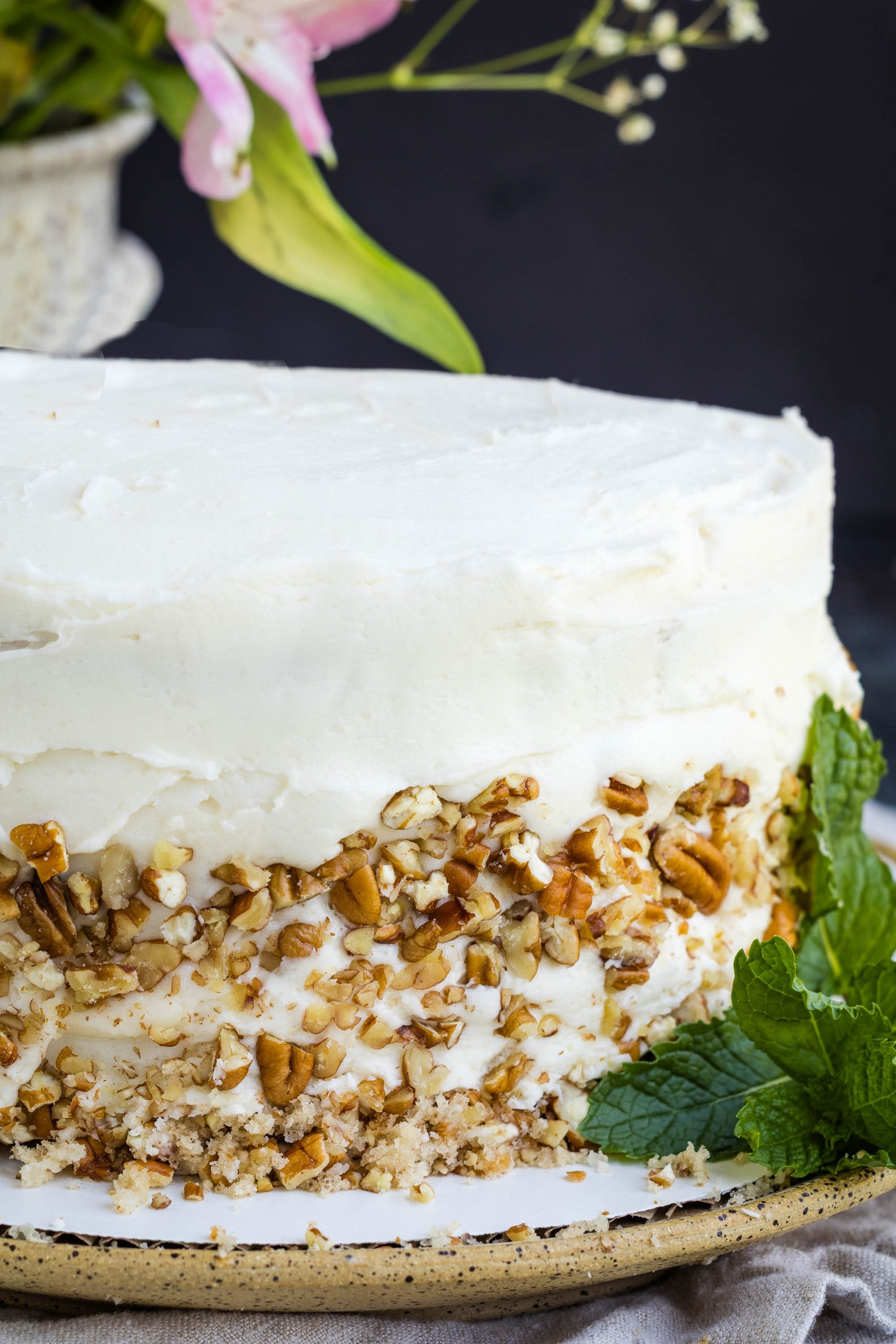 A frosted layer cake with chopped nuts pressed into the sides, garnished with fresh mint leaves and displayed on a plate.