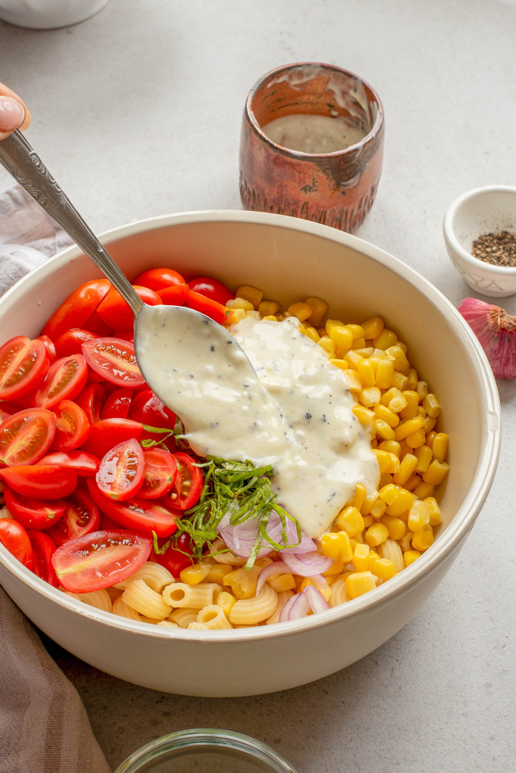 A bowl containing food with a spoon pouring creamy dressing on top.