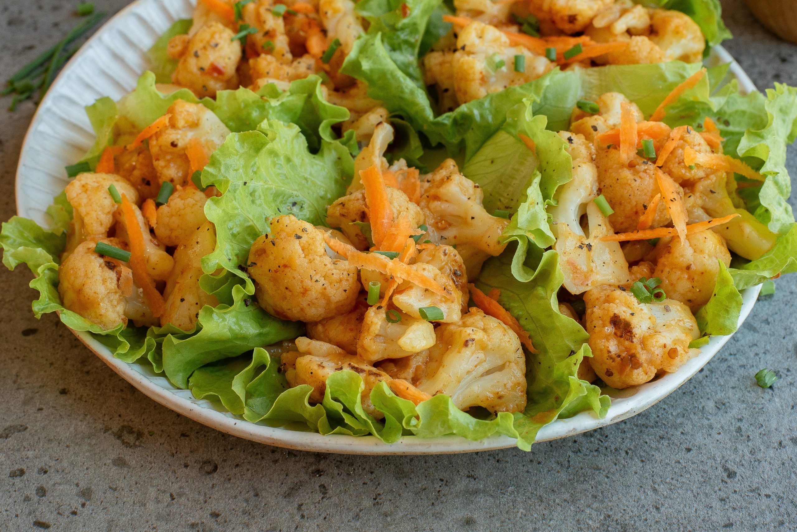 A plate of greens topped with spiced cauliflower florets and shredded carrots, garnished with chopped herbs.