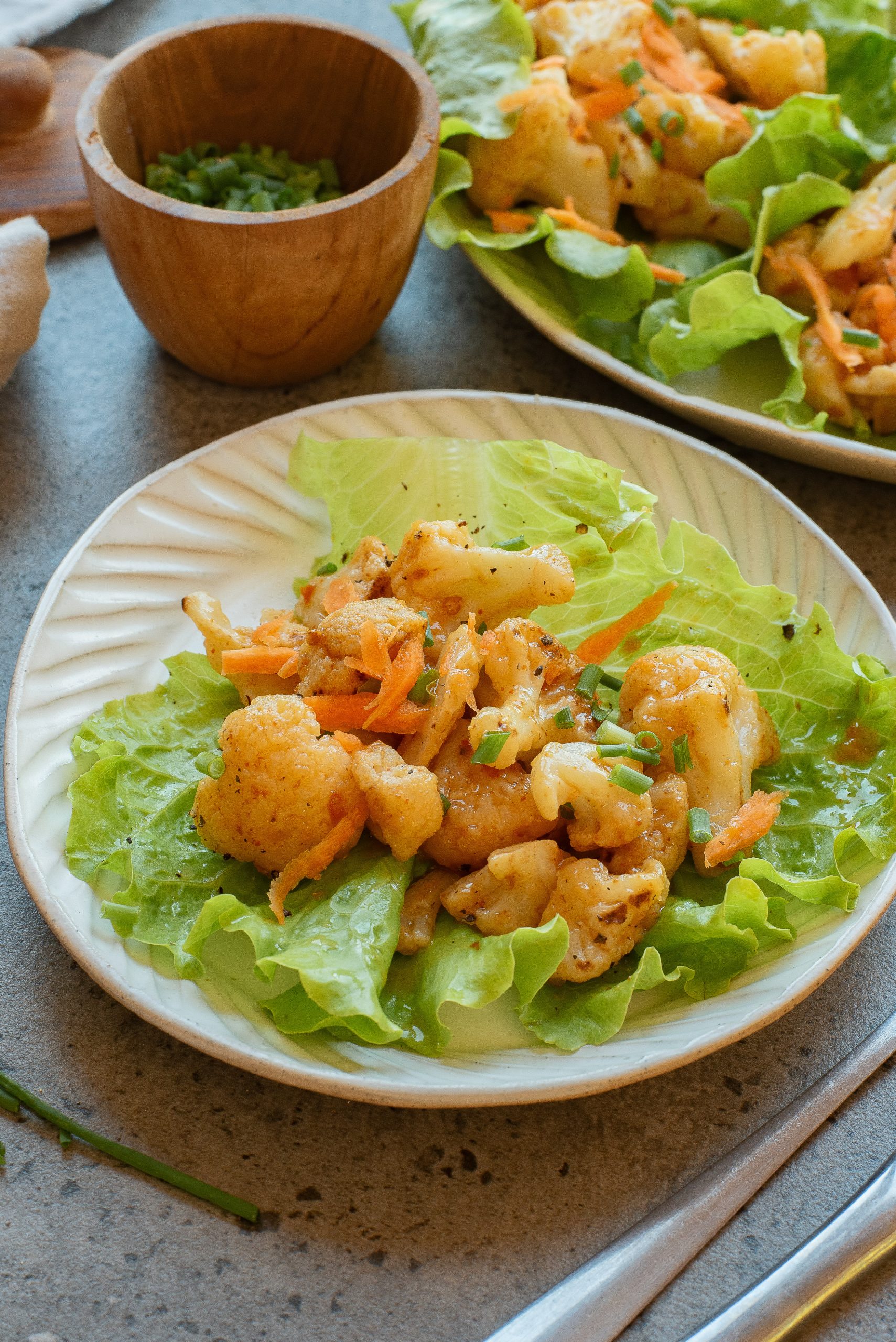 A plate of roasted cauliflower and shredded carrots served on green lettuce leaves, garnished with chopped chives.
