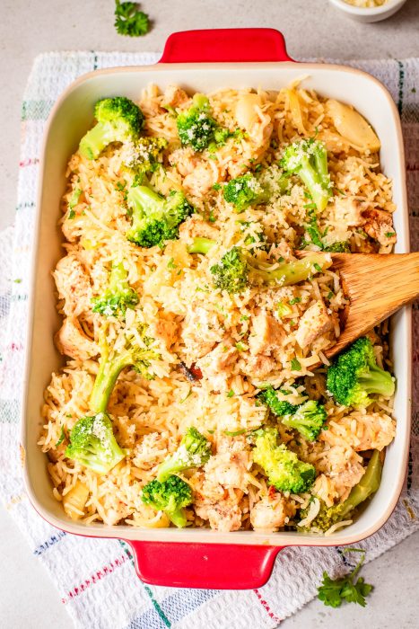 Baked casserole dish filled with rice, chicken, broccoli florets, and a wooden serving spoon resting inside.
