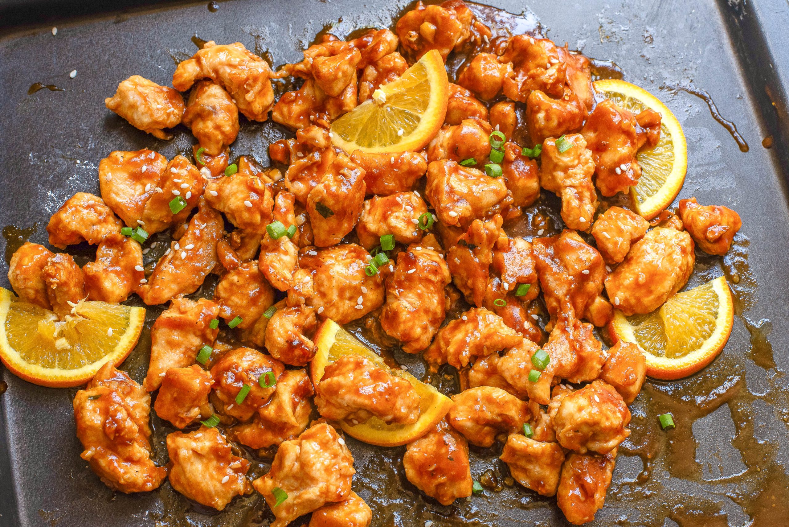Pieces of cooked protein garnished with sesame seeds and chopped green onions on a baking sheet.