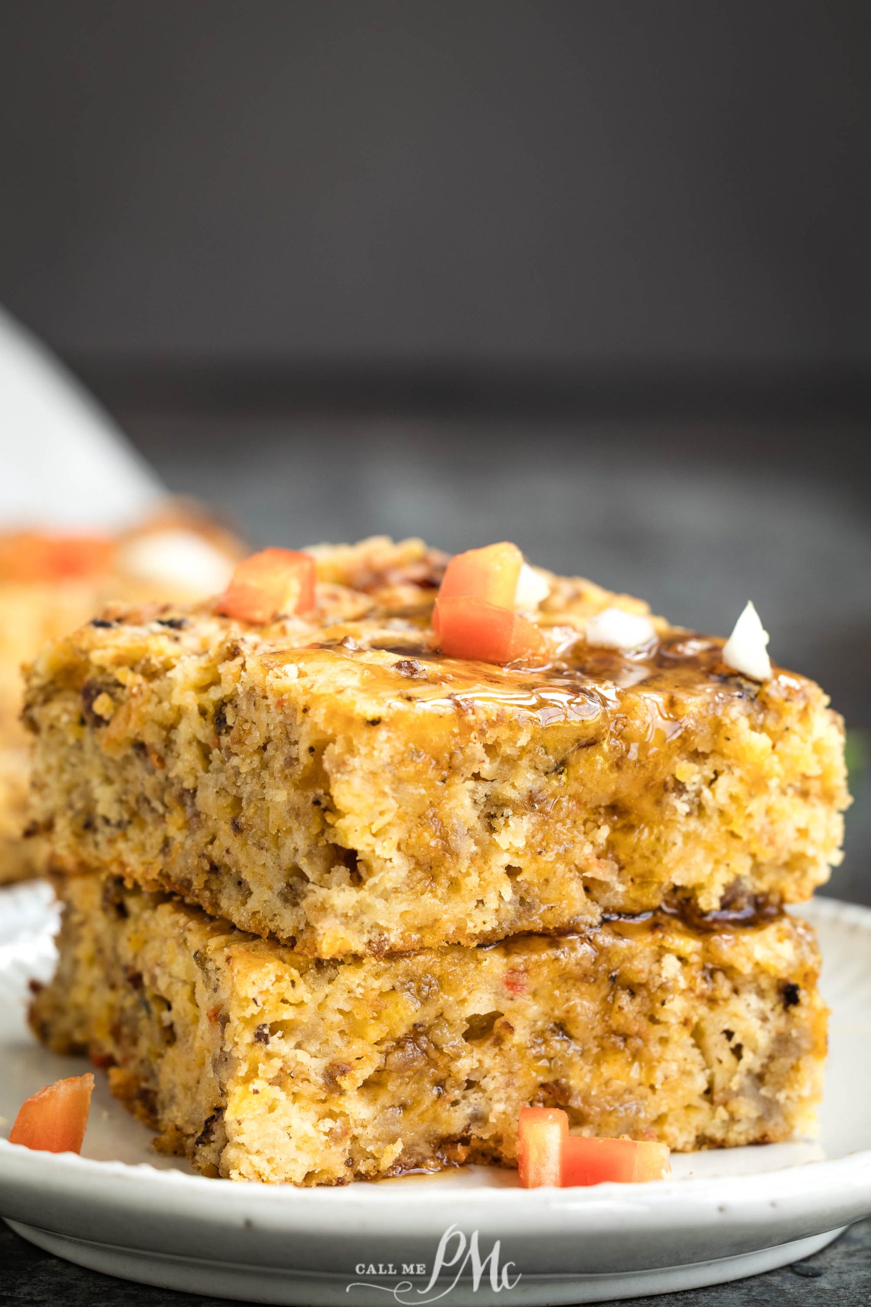 Two square pieces of savory sausage cheddar cake topped with chopped tomatoes and drizzled with a dark sauce, stacked on a white plate.