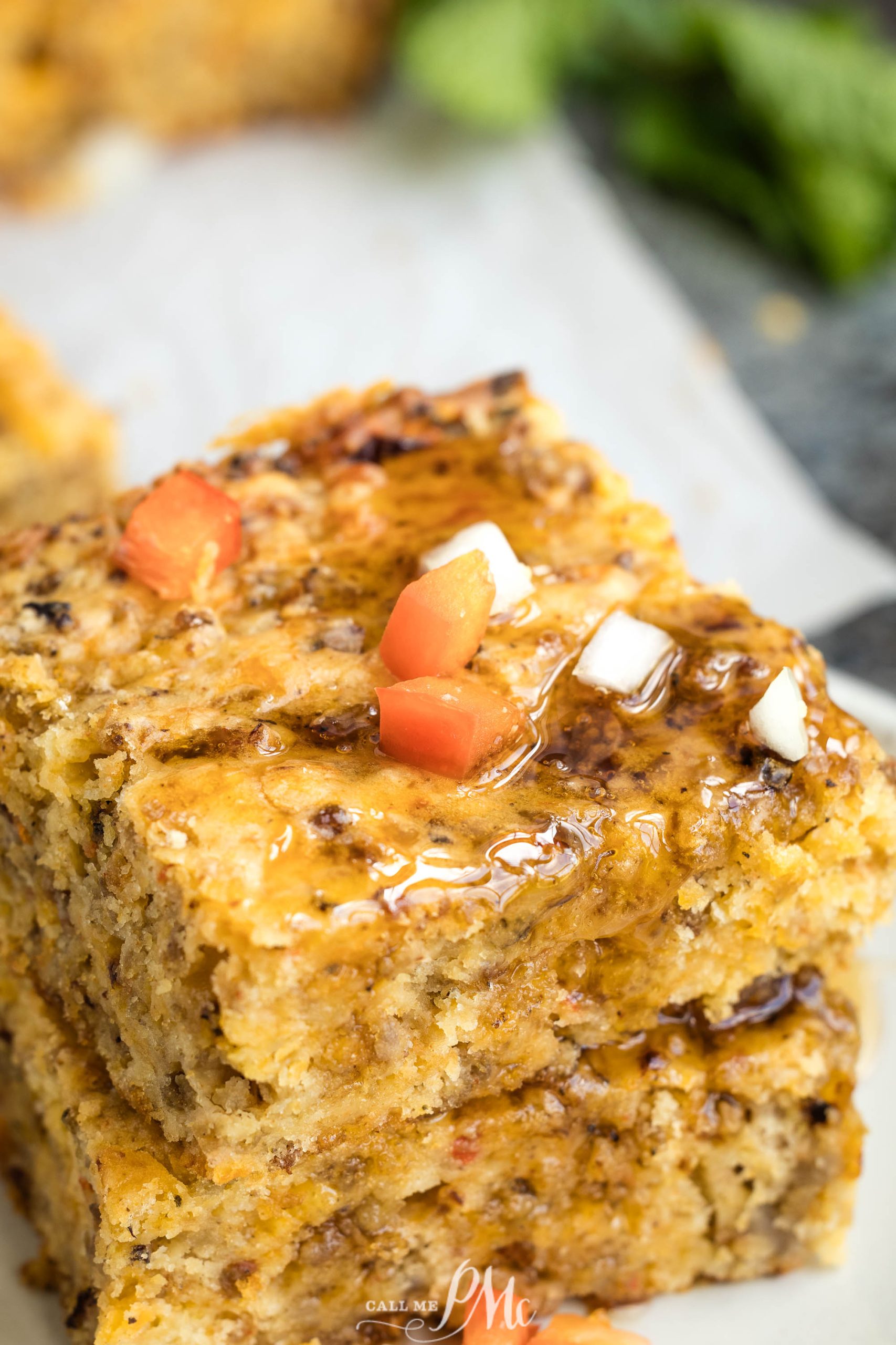 Two stacked pieces of sausage cake with syrup drizzled on top, garnished with small diced pieces of tomato and onion.