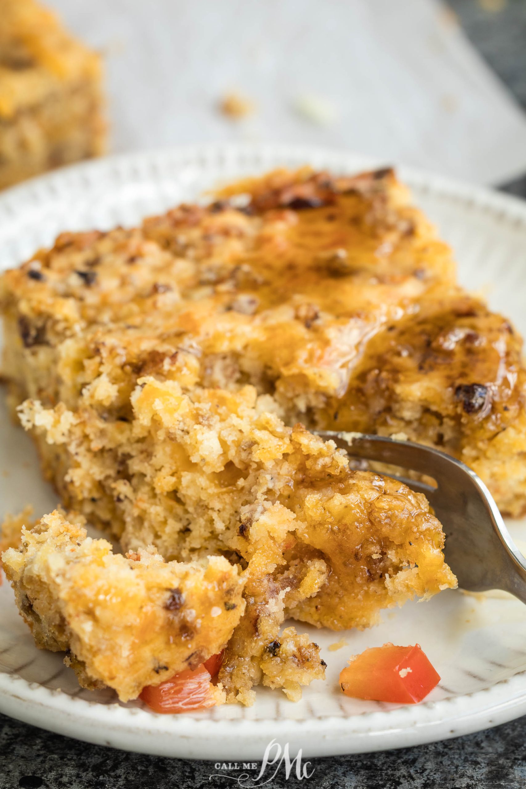 A close-up of a fork cutting into a slice of moist, crumbly cornbread with visible pieces of sausage and peppers on a white plate.
