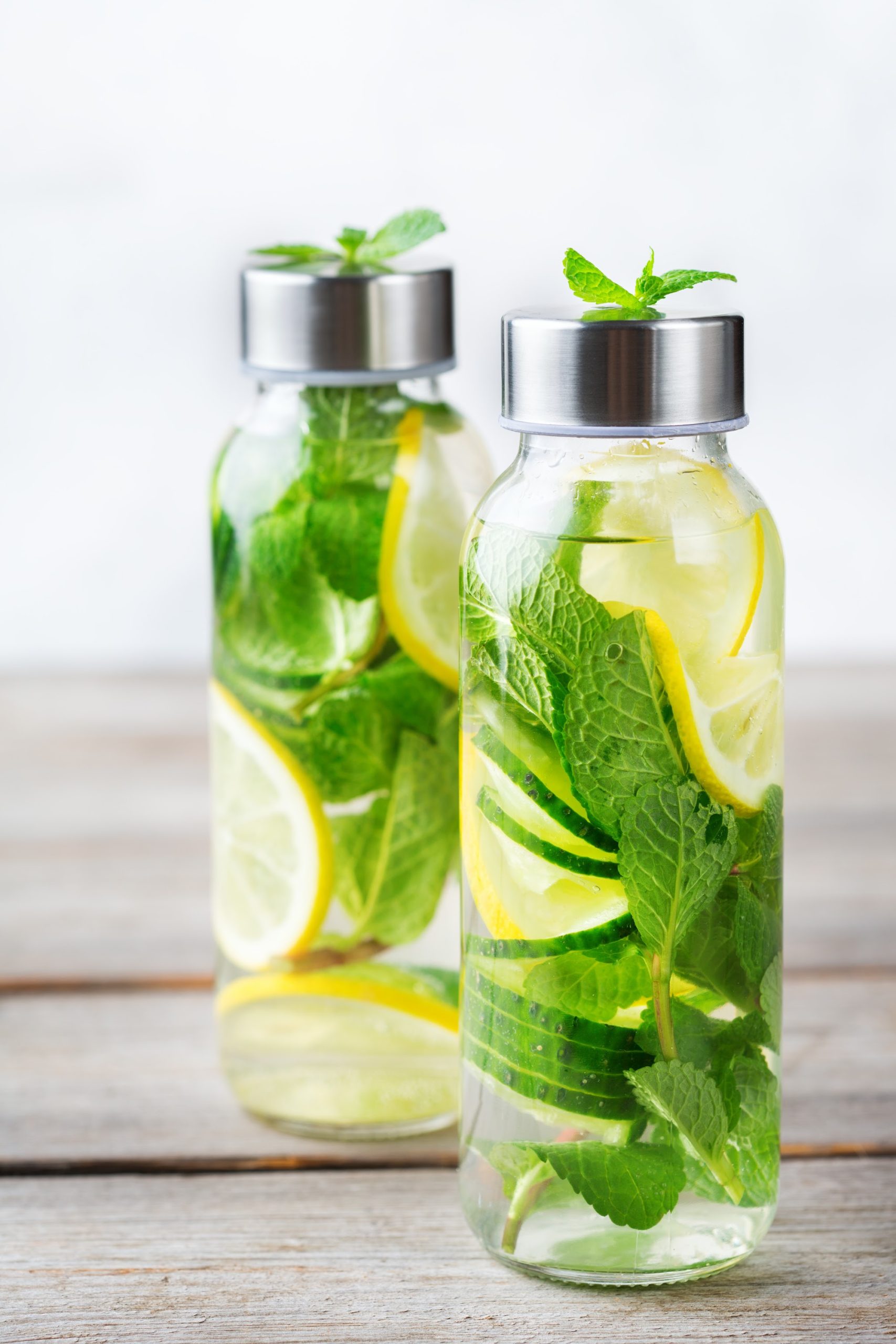 Two glass bottles filled with water, lemon slices, and fresh mint leaves—perfect for Fruit-Infused Water Recipes—are each topped with a metal lid and placed on a wooden surface.