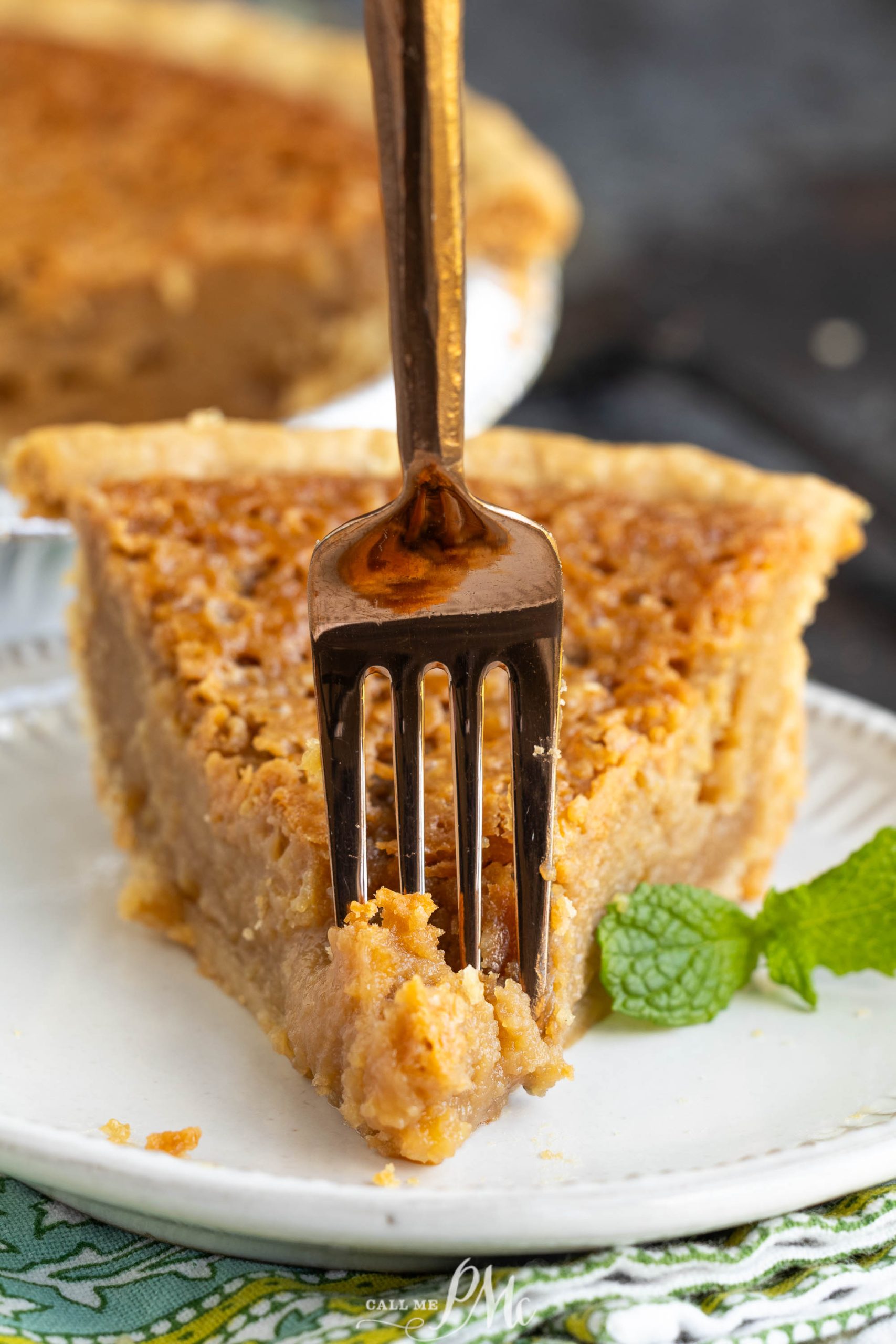 A fork cutting into a slice of light brown pie on a white plate, garnished with a sprig of mint.
