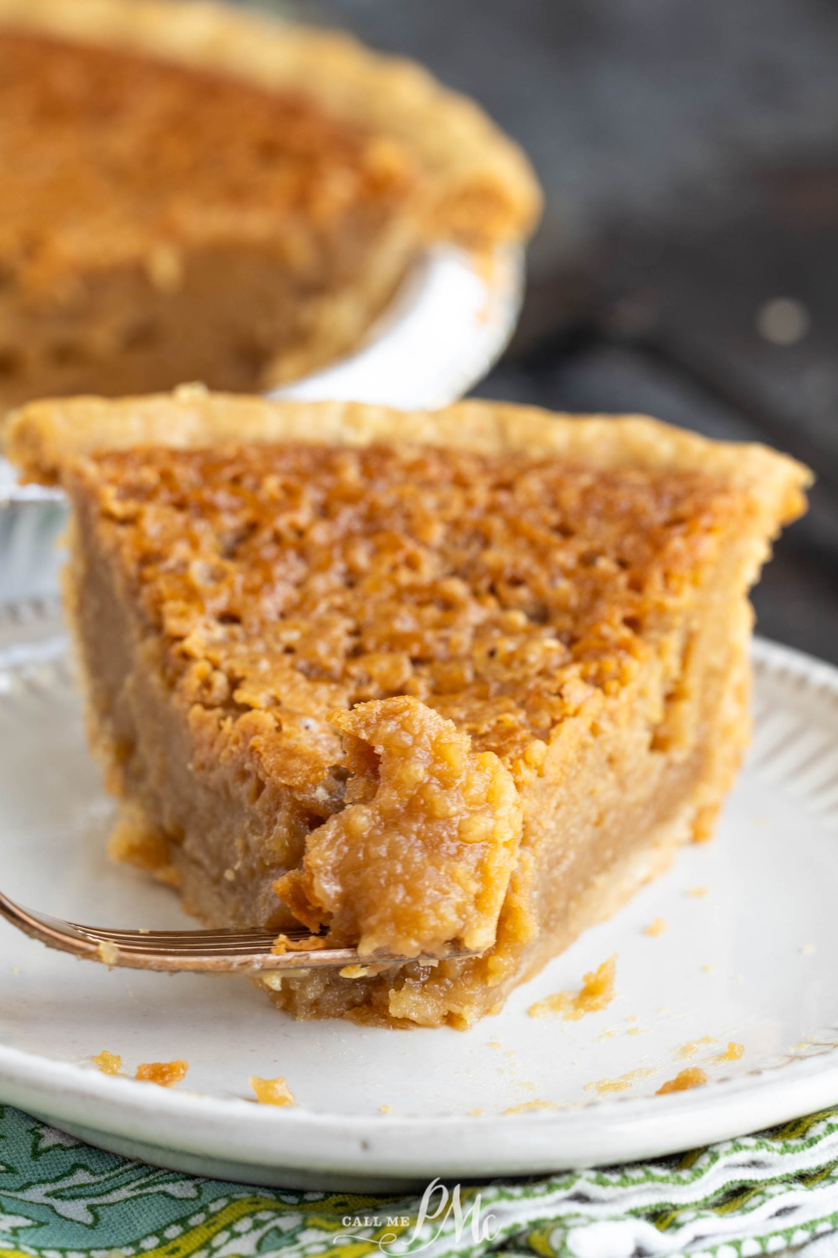 A close-up of a slice of brown pie with a flaky crust on a white plate, with a fork taking a bite from the front of the slice.