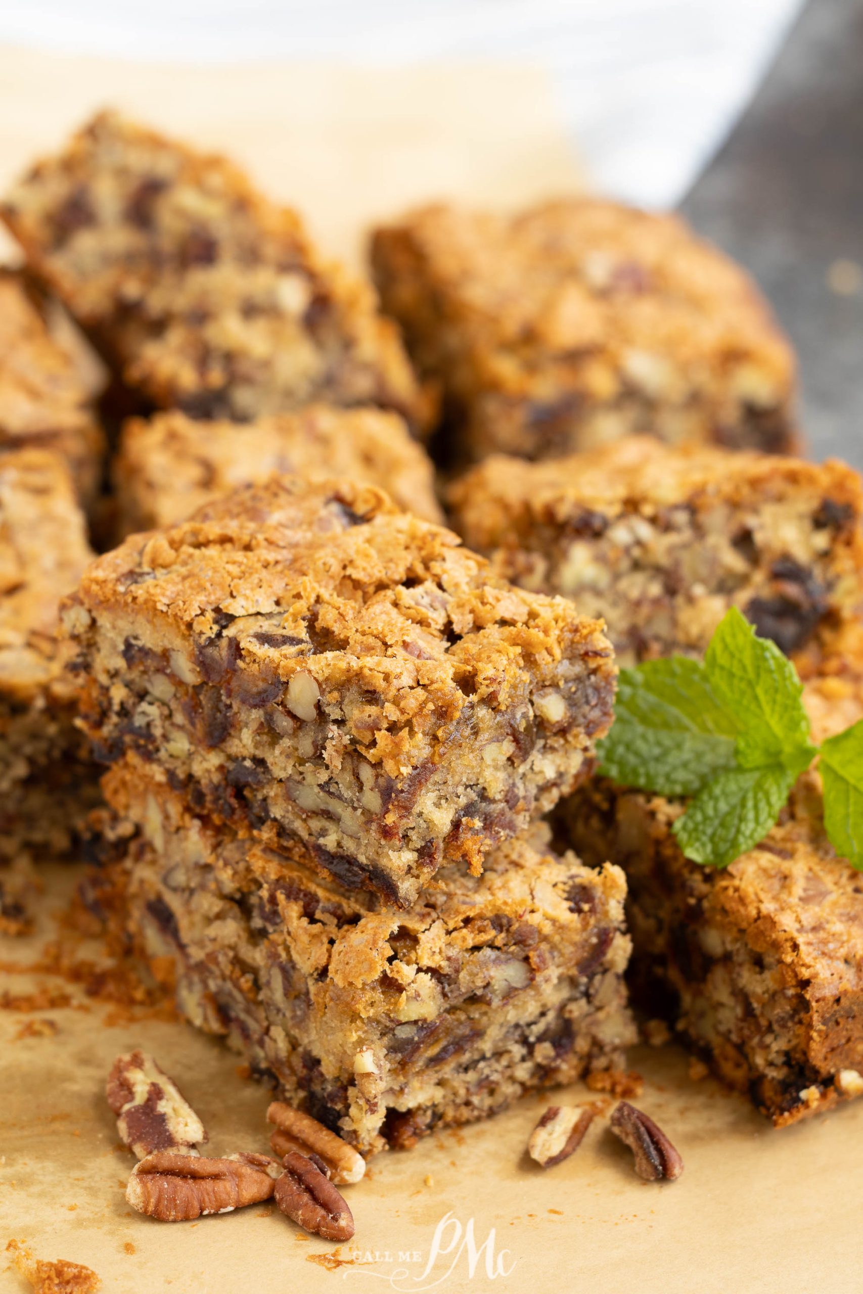 Stacked Old Fashioned Date Nut Bread with visible pecan pieces and a sprig of mint on top, resting on parchment paper with additional pecans in the foreground.