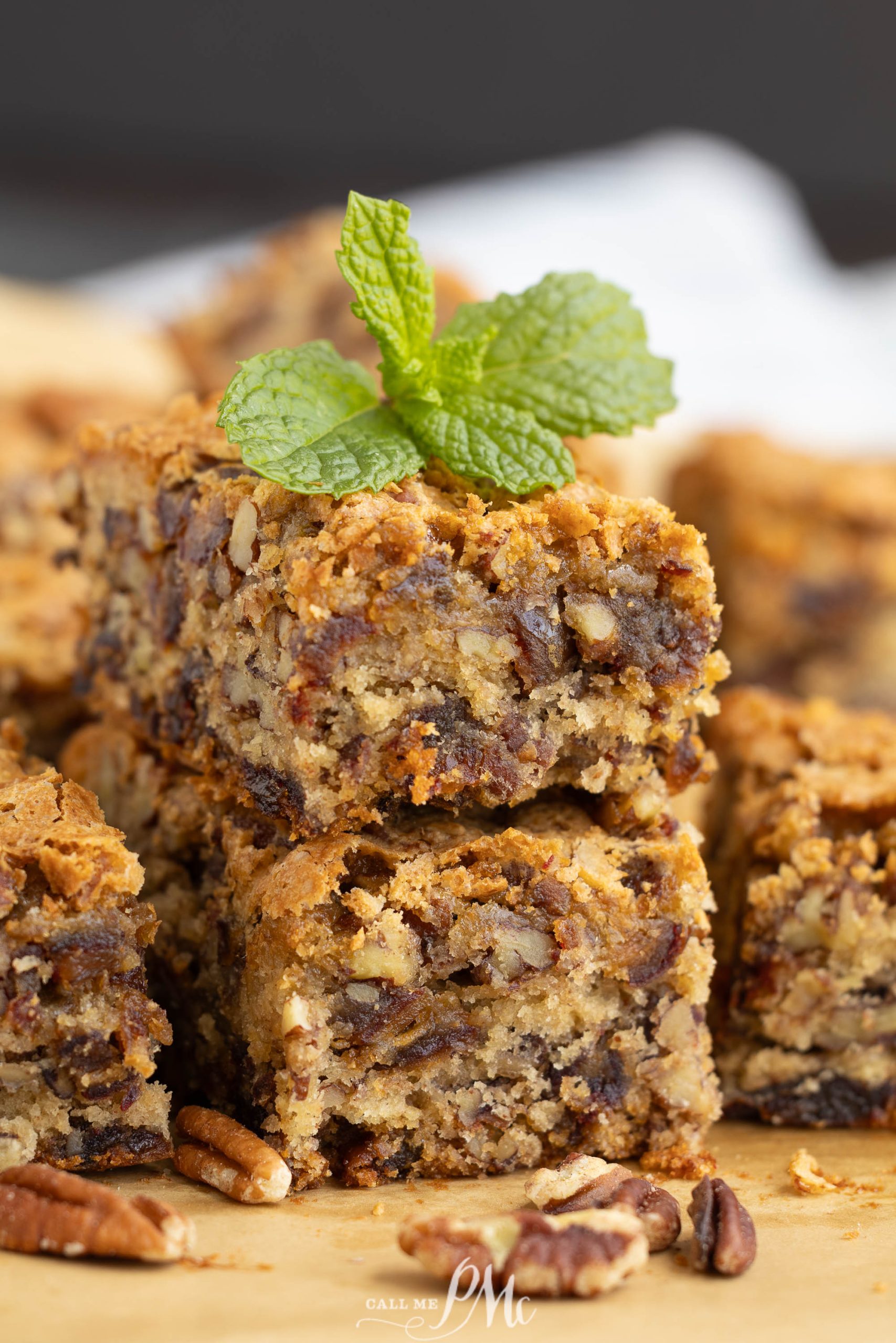 Close-up of stacked Old Fashioned Date Nut Bread topped with a sprig of fresh mint, surrounded by scattered pecan halves on a wooden surface.