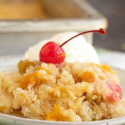 A serving of peach cobbler topped with a maraschino cherry and a scoop of vanilla ice cream, served on a plate.