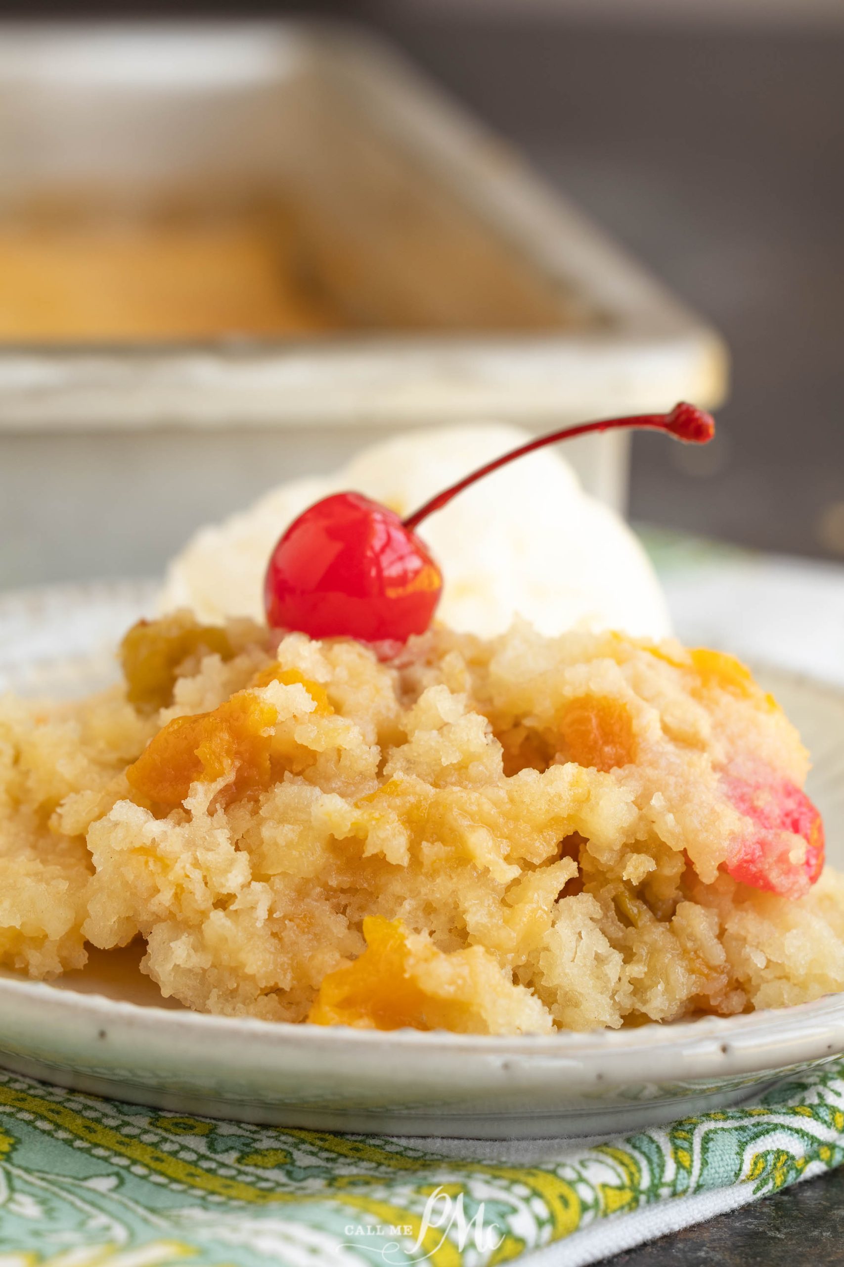 A serving of peach cobbler topped with a maraschino cherry and a scoop of vanilla ice cream, served on a plate.