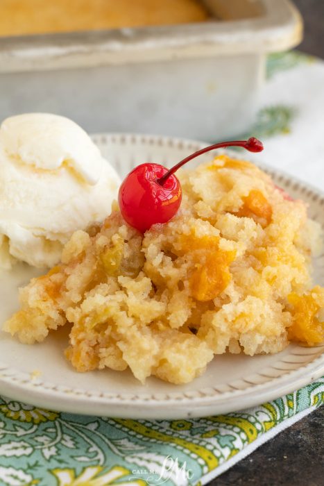 A serving of peach cobbler topped with a maraschino cherry, alongside a scoop of vanilla ice cream on a plate.