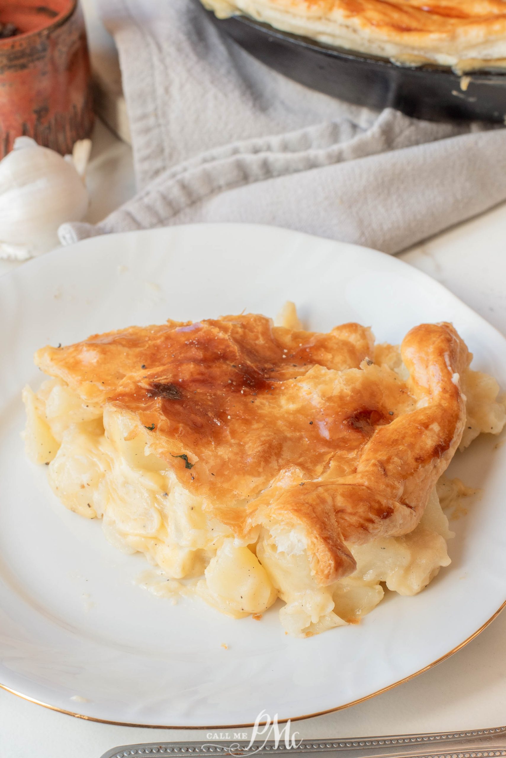 A slice of Potato Cheese Onion Pot Pie with flaky crust on a white plate, set on a table with a beige napkin nearby.