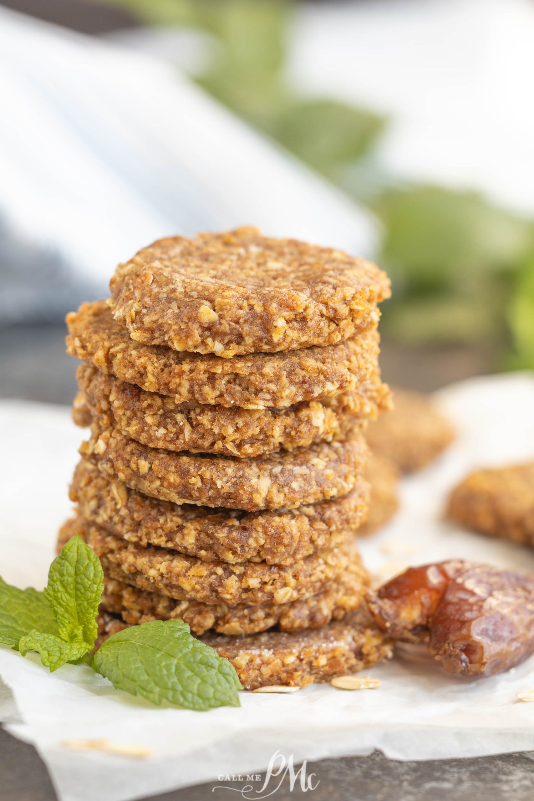 A stack of round treats sits on parchment paper next to a sprig of mint and a date.