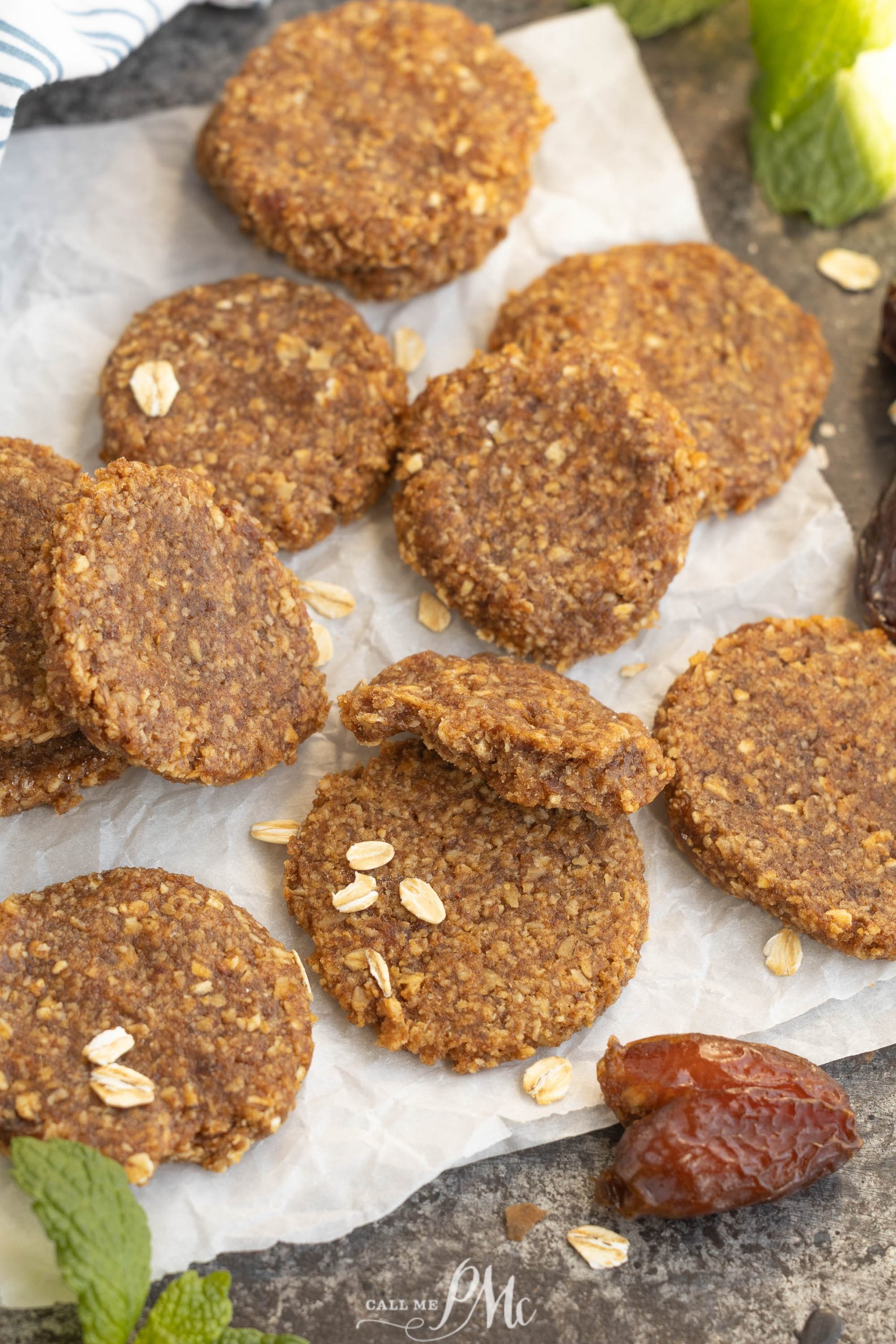 Round treats are arranged on parchment paper, with a few oats scattered on top and dates and mint leaves nearby.