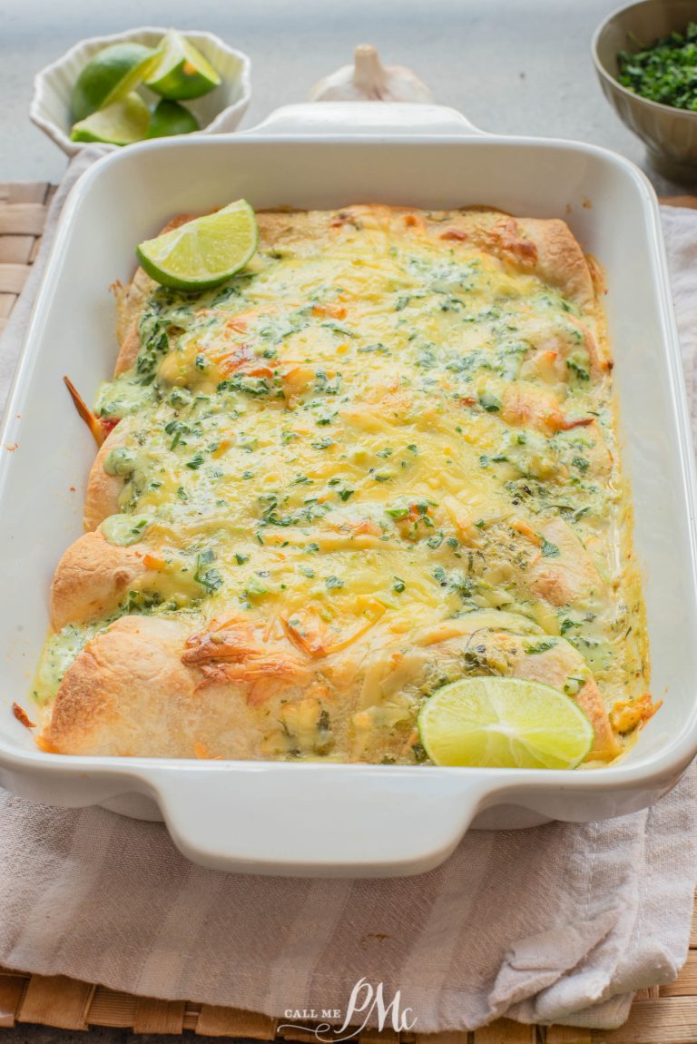 A baked casserole dish filled with cheesy enchiladas, topped with chopped herbs and lime wedges, sits on a cloth napkin.
