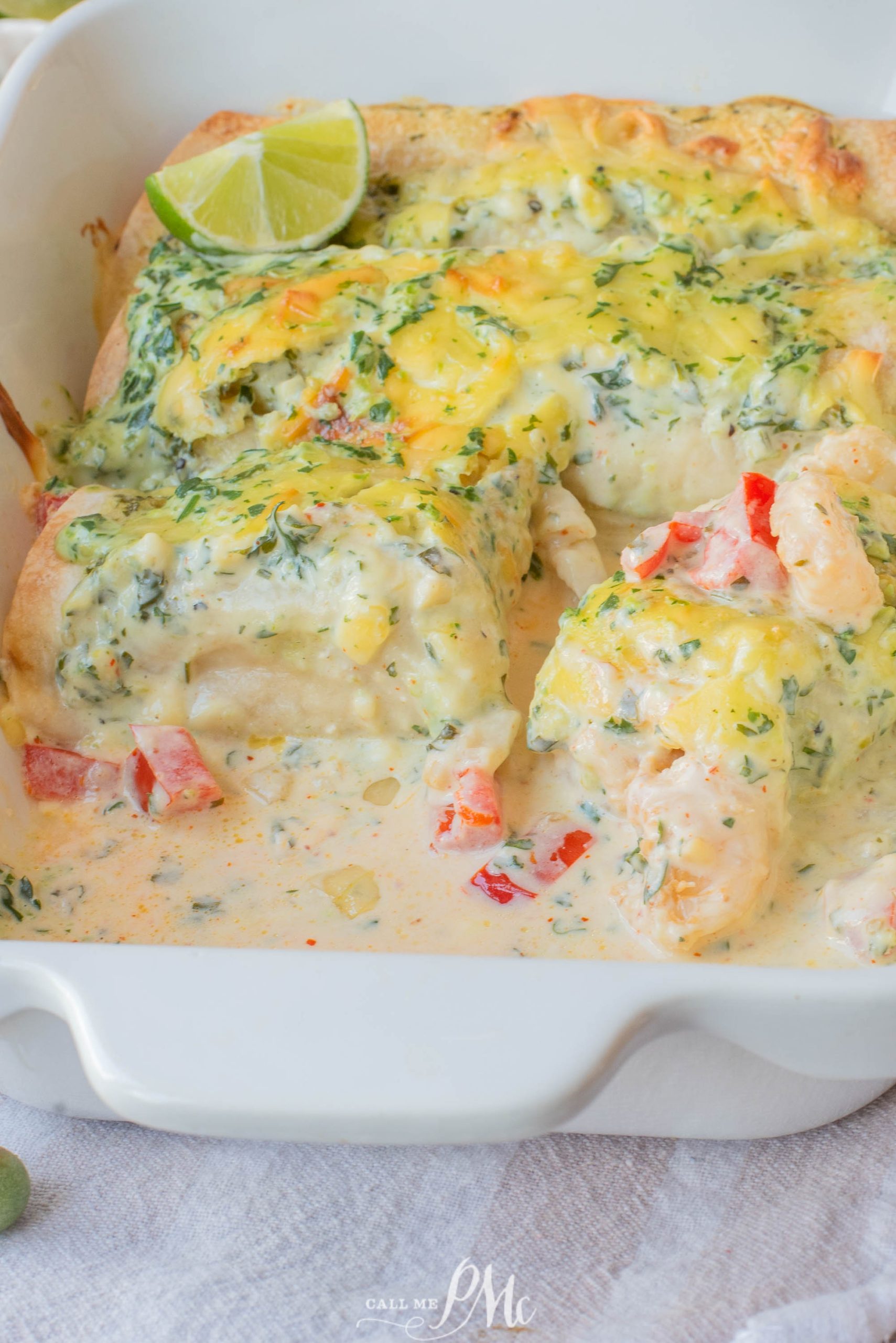 Baked creamy chicken enchiladas topped with cheese and cilantro, sliced in a white dish, with a lime wedge for garnish.