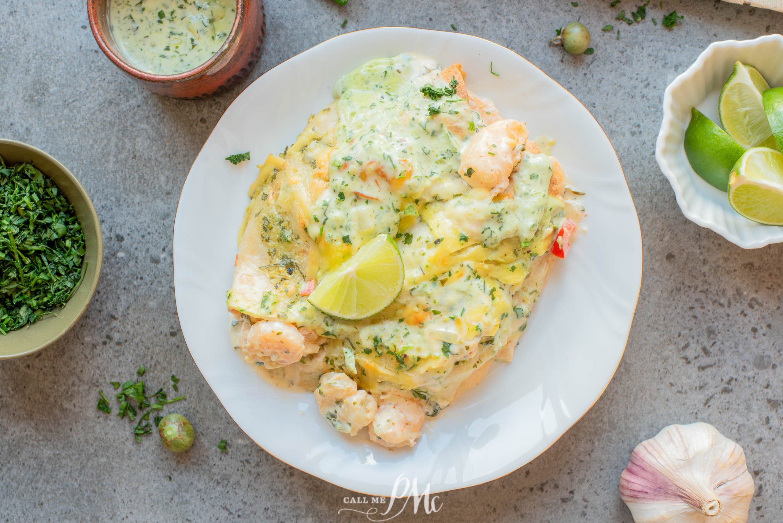 A plate of Low-carb shrimp enchiladas covered in creamy herb sauce, garnished with a lime wedge, with bowls of fresh herbs, sauce, and lime on the side.