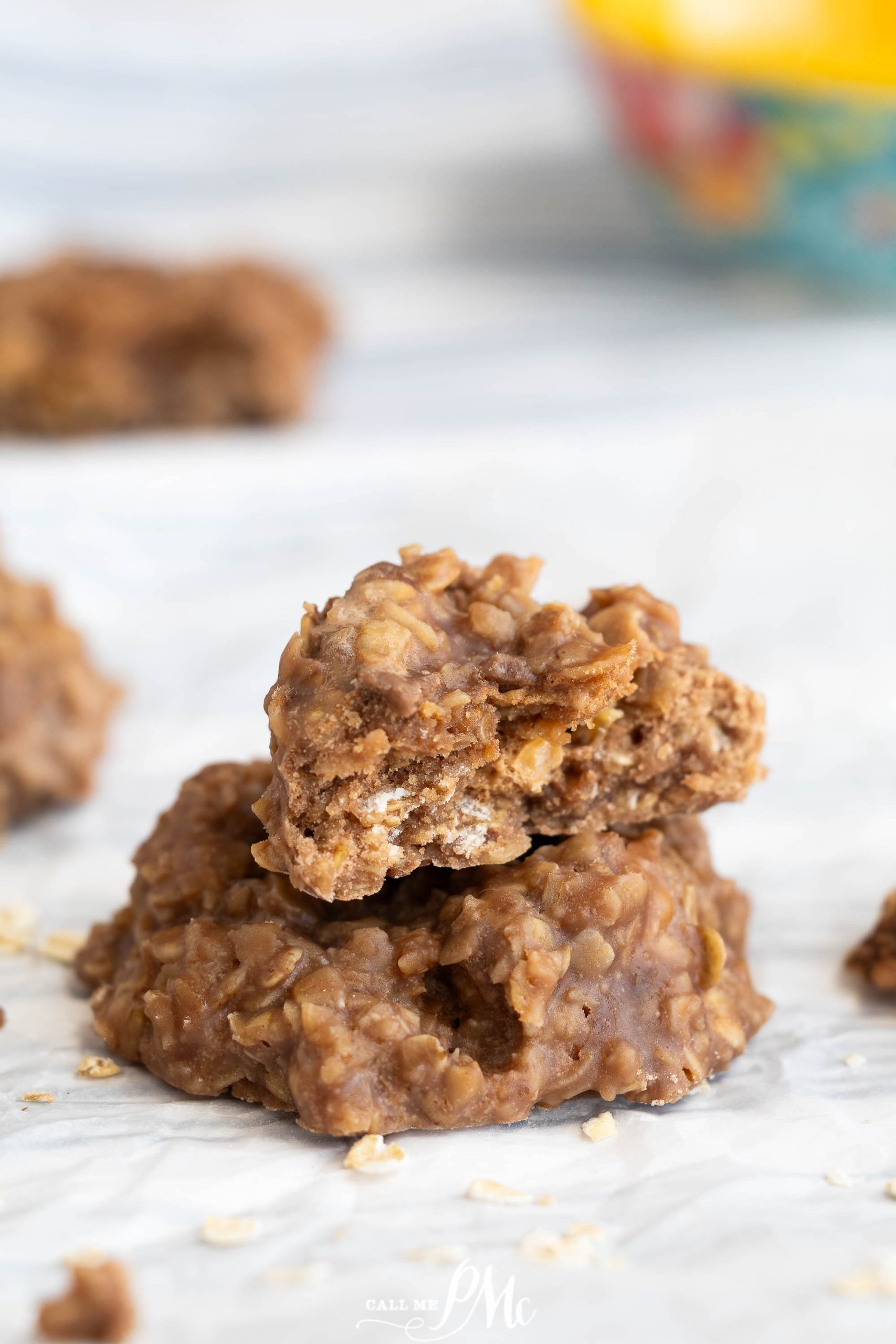 Two no-bake chocolate oatmeal cookies stacked on parchment paper, with the top cookie partially bitten.
