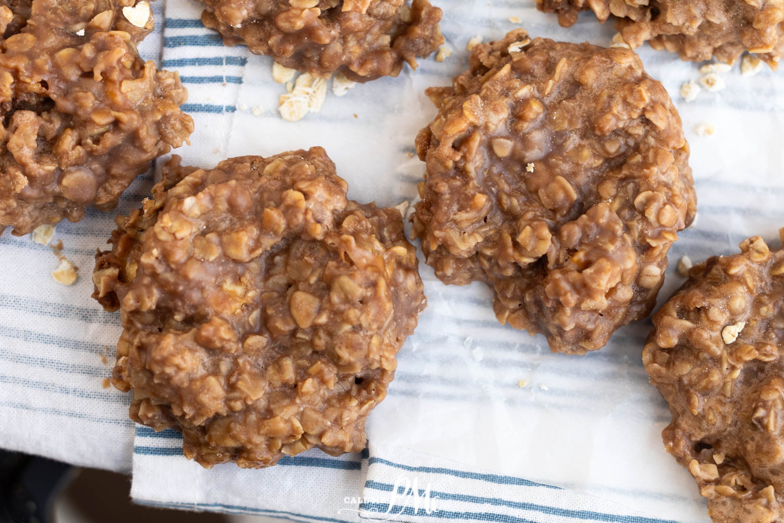 Close-up of several no-bake chocolate oatmeal cookies on a striped cloth and parchment paper.