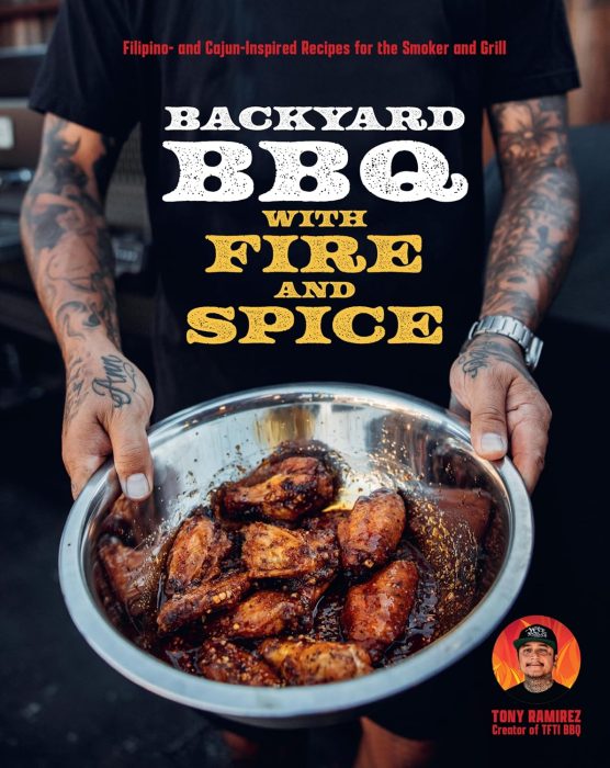 A person holds a metal bowl filled with seasoned grilled chicken wings in front of a BBQ grill; "Backyard BBQ with Fire and Spice" is the book title—perfect for fans of outdoor cooking gifts.