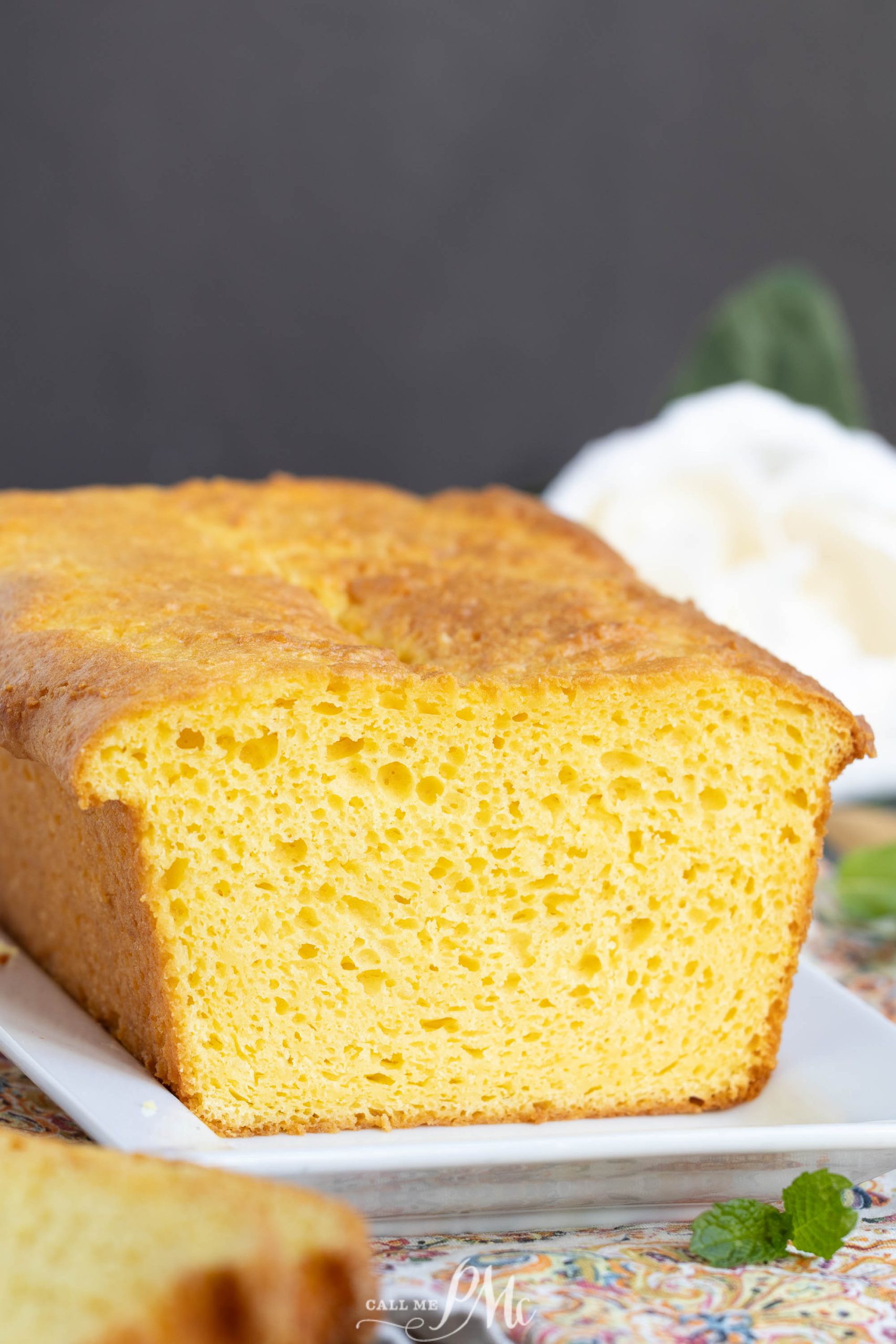 A loaf of sliced, golden-yellow bread sits on a white rectangular plate, showing its airy texture and slightly browned crust.