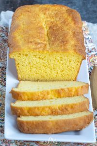 A loaf of cornbread with several slices cut and arranged on a white rectangular plate.