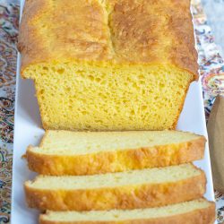 A loaf of cornbread with several slices cut and arranged on a white rectangular plate.