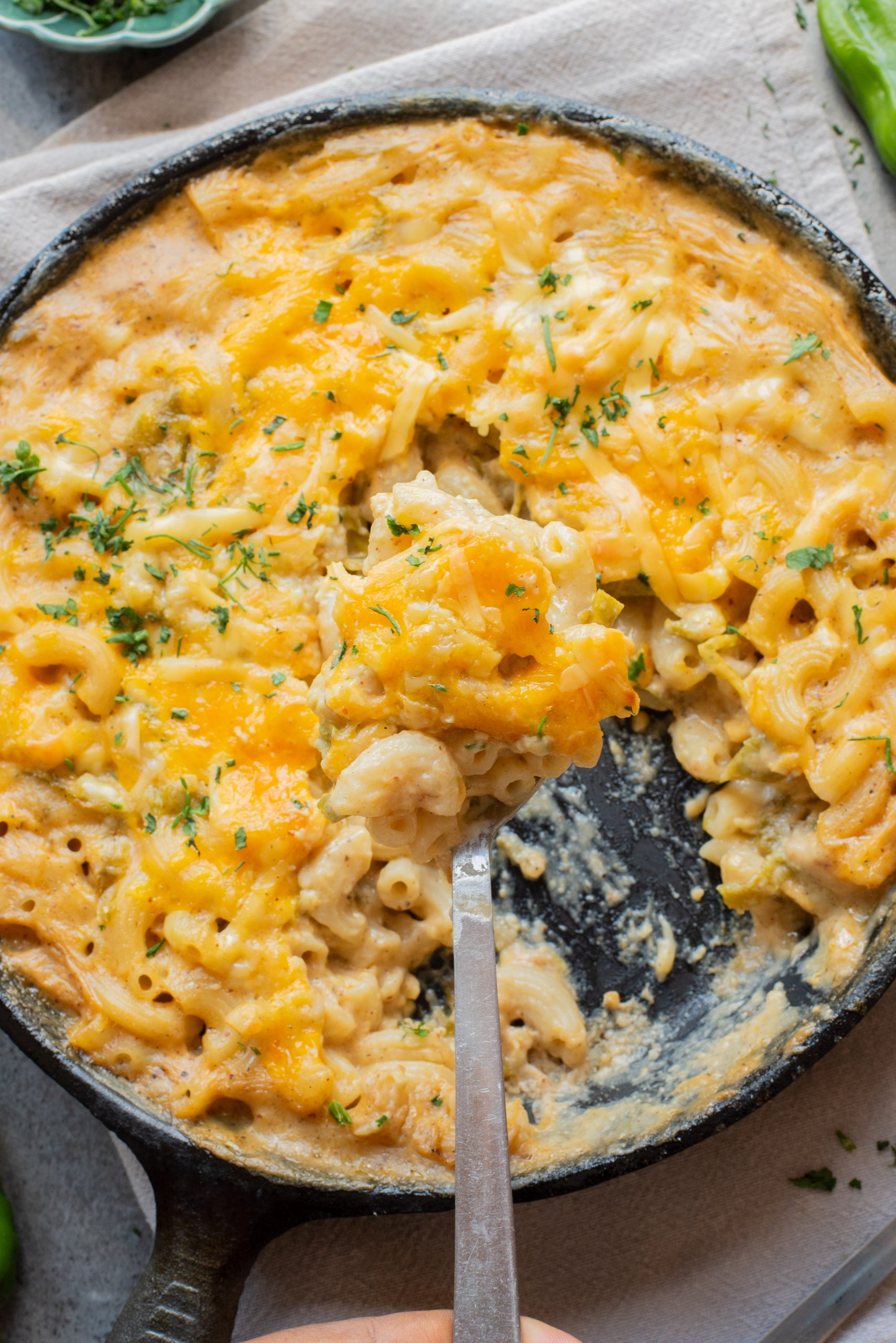 A skillet filled with baked macaroni and cheese, partially served, topped with melted cheddar and garnished with chopped herbs.
