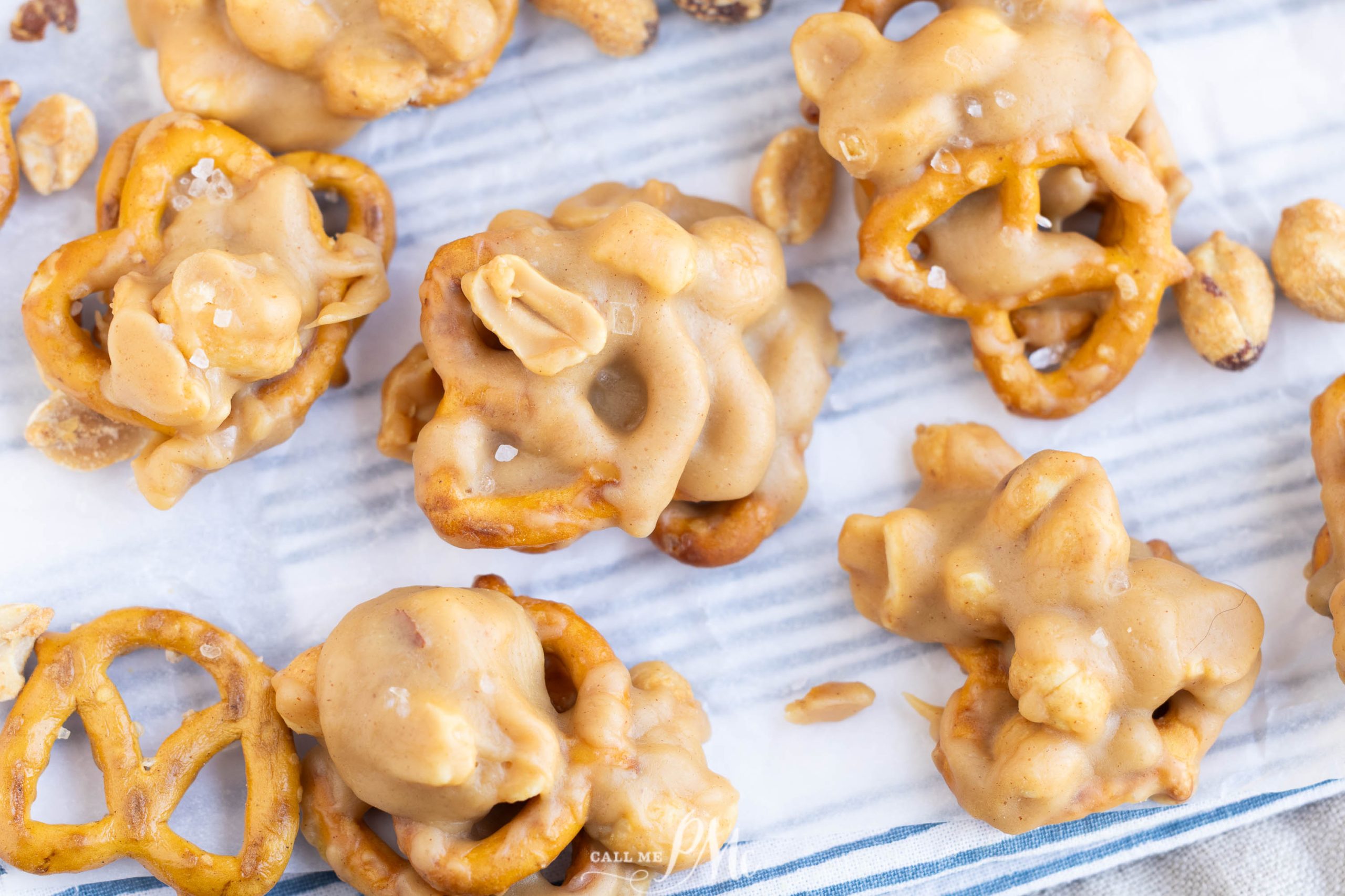 Clusters of pretzels and peanuts coated in a creamy, light brown candy mixture are arranged on a piece of parchment paper.
