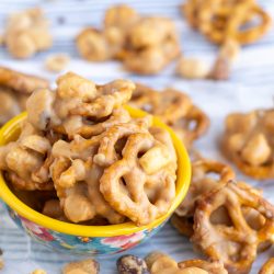 A small bowl filled with clusters of pretzels coated in a caramel-like glaze, surrounded by more glazed pretzel clusters on a striped surface.
