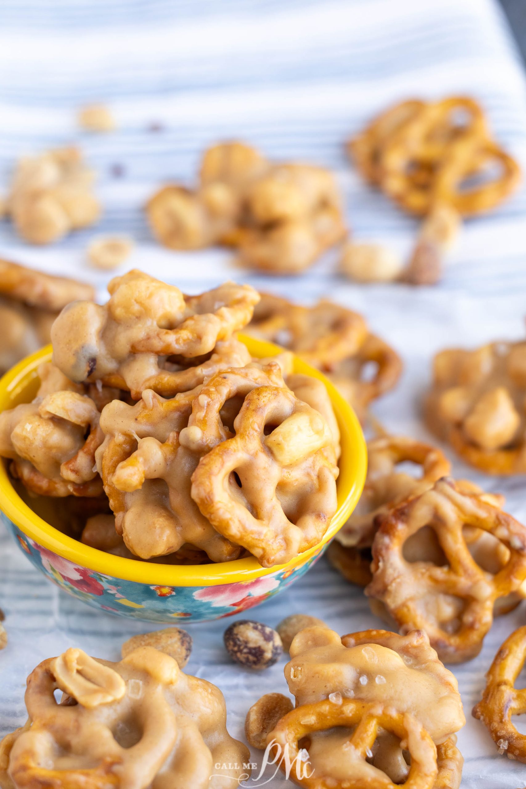 A small bowl filled with clusters of pretzels coated in a caramel-like glaze, surrounded by more glazed pretzel clusters on a striped surface.