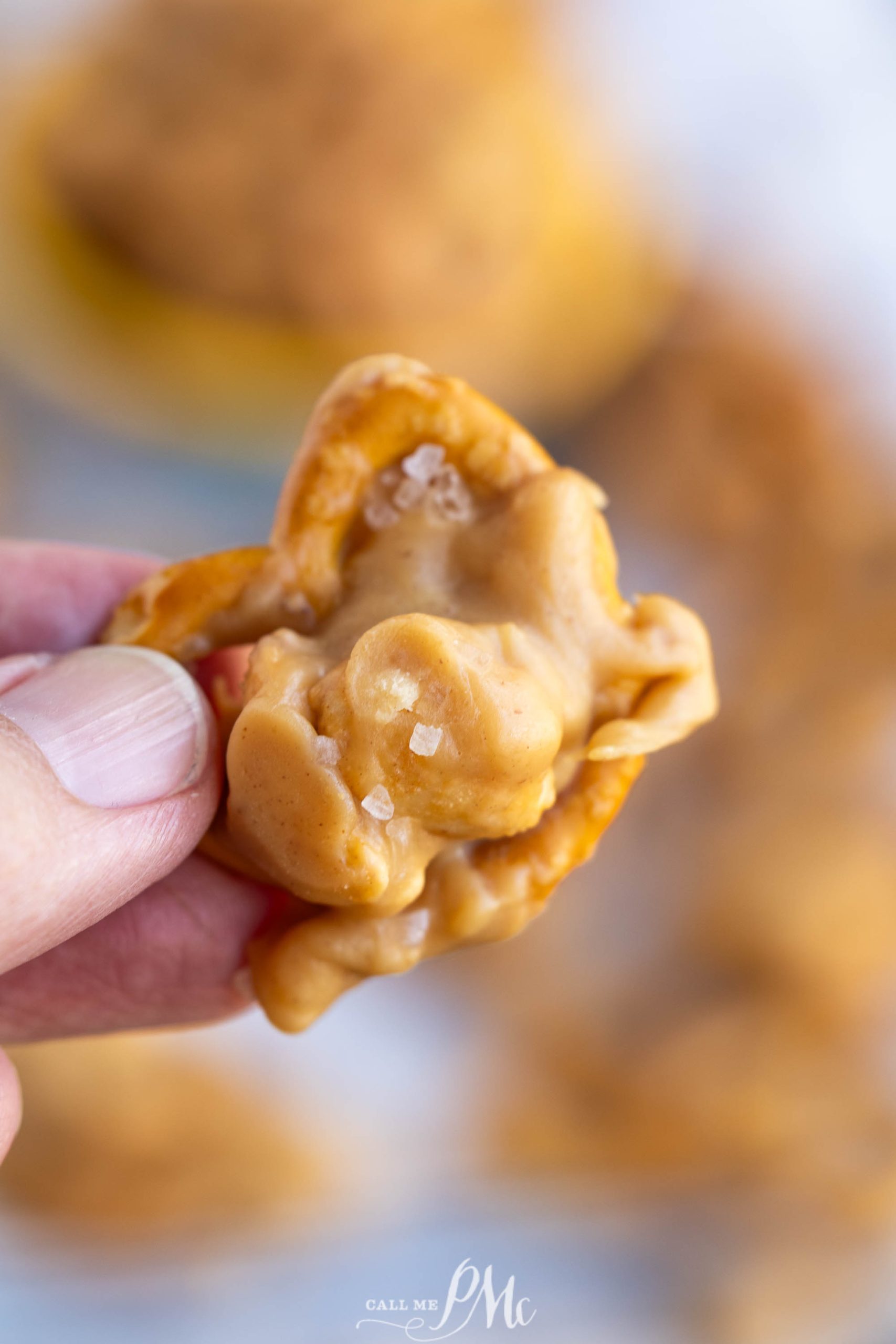 A hand holding a pretzel topped with a creamy peanut butter mixture and a sprinkle of sea salt.