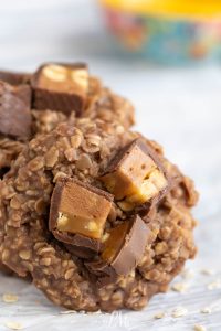 A no-bake oatmeal cookie topped with chopped pieces of chocolate and caramel candy, shown in close-up on a light background.